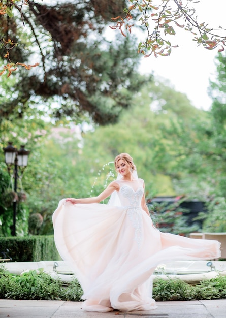 Charmante mariée dans une robe de pêche tourbillonne avant fontaine dans le jardin