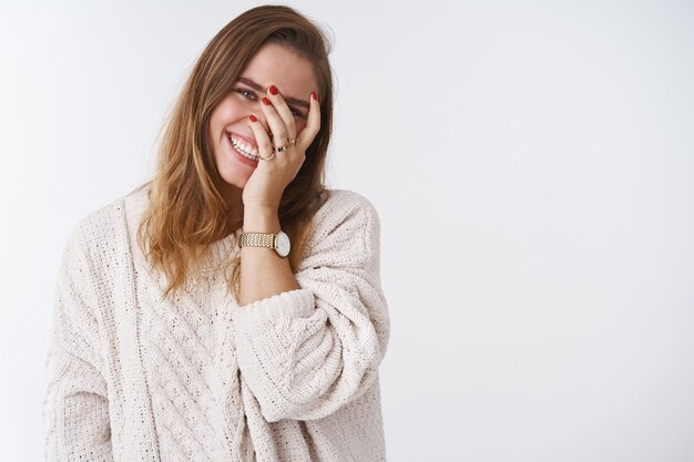 Charmante petite amie adulte caucasienne mignonne affectueuse mignonne inclinant la tête face à la paume de la main idiot jetant un coup d'œil à travers les doigts en riant à haute voix s'amusant à rougir en regardant amusé joyeux fond blanc