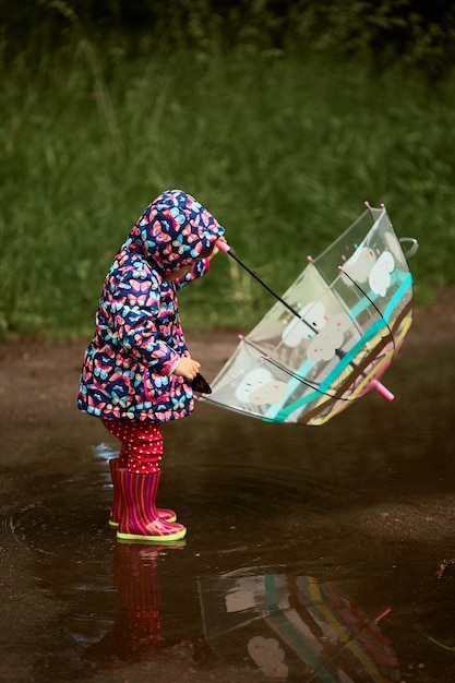 Charmante petite fille avec un parapluie s&#39;amuse debout dans des bottes en caoutchouc dans la piscine après la pluie