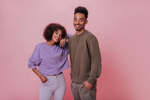 Photo gratuite charmants amis masculins et féminins souriants sur fond rose femme en sweat-shirt violet et homme en tenue marron regardent la caméra