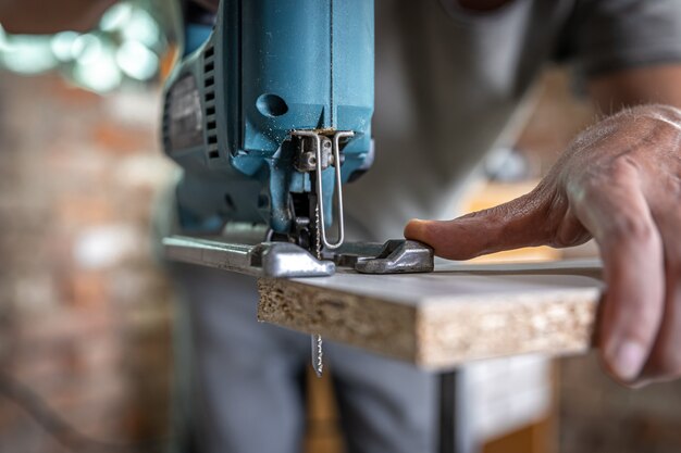 Un charpentier coupe un bois avec une scie sauteuse électrique, travaillant avec un arbre.