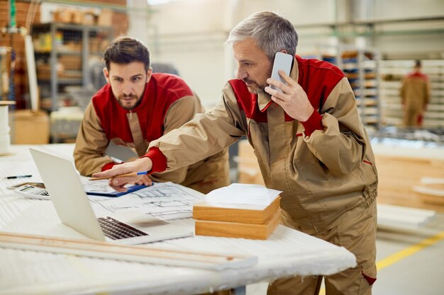 Charpentier parlant au téléphone tout en utilisant l'ordinateur dans un atelier