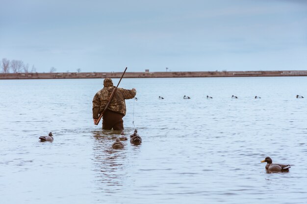 Chasseur avec un fusil sur le dos faisant une pause dans la chasse et attrapant un poisson dans un lac avec des canards