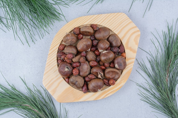 Photo gratuite châtaignes et cynorrhodons séchés sur plaque en bois.