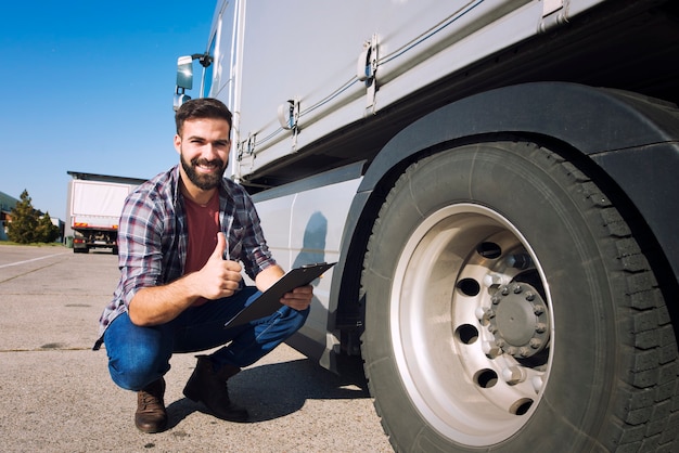 Photo gratuite chauffeur de camion avec les pouces vers le haut inspectant l'état des pneus et vérifiant la pression