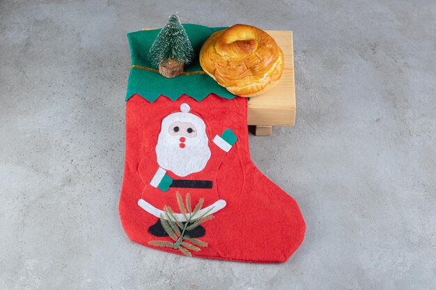 Chaussette avec illustration de père Noël, chignon sucré et une petite figurine d'arbre sur table en marbre.