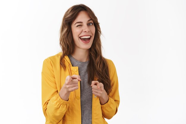 Cheeky confiant détendue jeune femme du parti souriant largement clignant de l'approbation pointant sur les pistolets à doigt avant vous beau geste de travail approuver un excellent choix, mur blanc