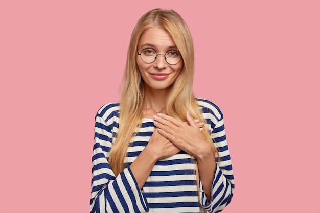 Cheerful blonde woman posant contre le mur rose