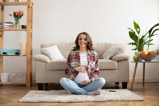 Cheerful brunette femme enceinte en chemise à carreaux rouge sourit sincèrement et touche doucement le ventre