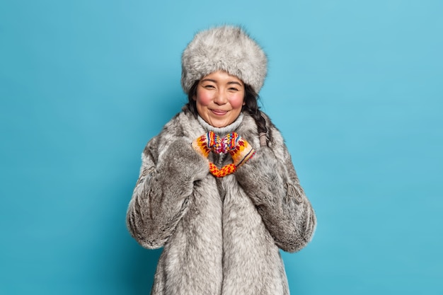 Photo gratuite cheerful eskimo woman formes coeur geste exprime l'amour vêtu de vêtements d'hiver chauds isolés sur mur bleu