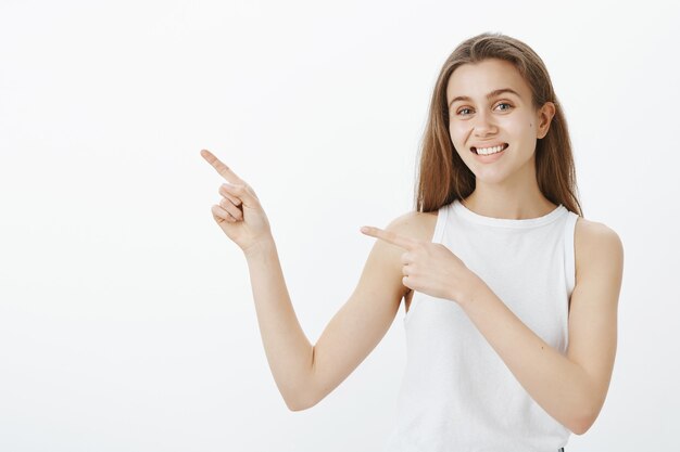 Cheerful girl student pointant le doigt dans le coin supérieur gauche, montrant la bannière de cours et souriant