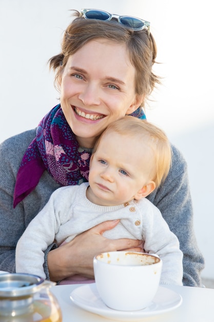 Cheerful mom holding sweet baby dans les bras tout en buvant du café dans un café