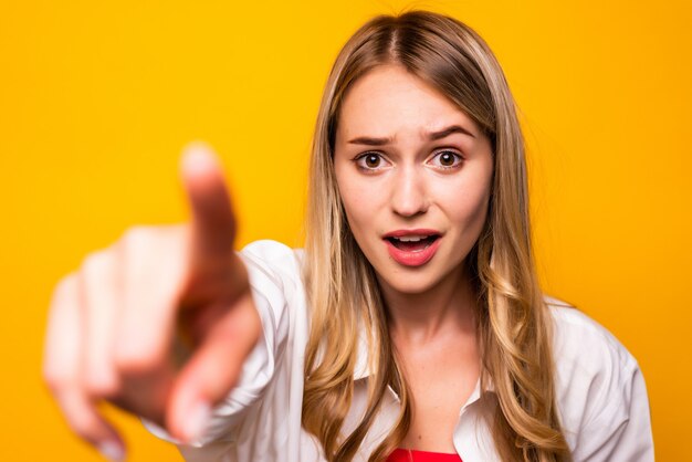 Cheerful woman in t-shirt pointant avec la bouche ouverte sur le mur jaune