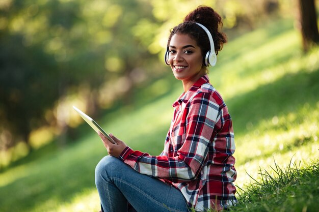 Cheerful young african woman sitting outdoors dans le parc