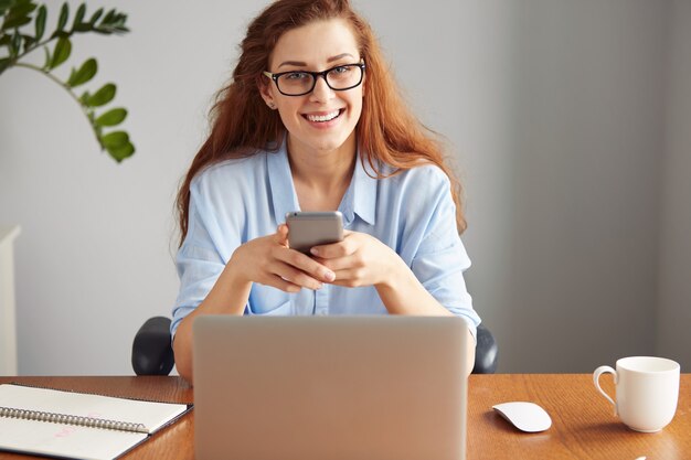 Cheerful young businesswoman travaillant sur ordinateur portable alors qu'il était assis sur son lieu de travail