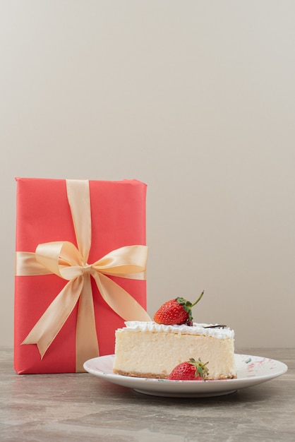 Cheesecake aux fraises et un cadeau sur table en marbre.