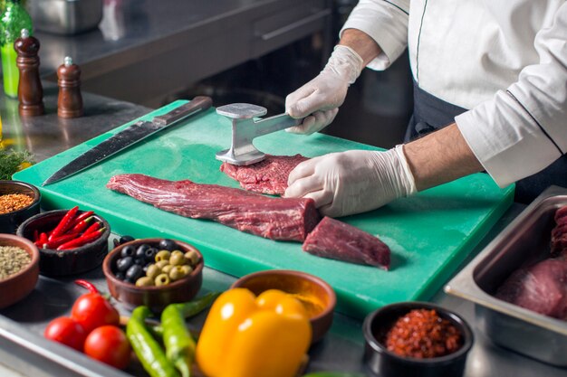 Chef attendrir steak avec attendrisseur de viande sur une planche à découper