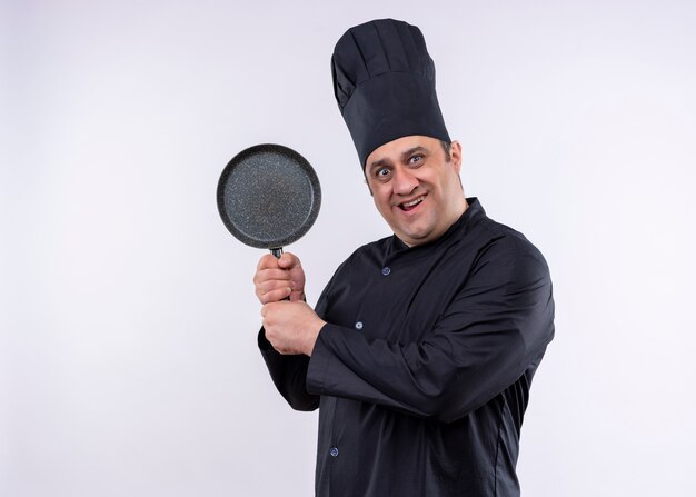 Chef cuisinier mâle portant l'uniforme noir et chapeau de cuisinier montrant pan loking à la caméra surpris et excité debout sur fond blanc