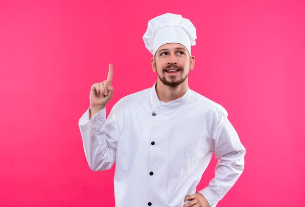 Chef cuisinier professionnel en uniforme blanc et chapeau de cuisinier à la recherche de pointage avec le doigt se rappelant de ne pas oublier la chose importante debout sur fond rose