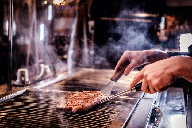 Chef cuisinier en uniforme cuisinant un délicieux steak de boeuf dans une cuisine d'un restaurant
