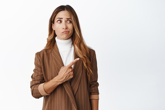 Chef de la direction adulte sceptique patronne dans l'entreprise pointant vers la droite regardant avec une expression de visage désabusée déçue debout sur fond blanc