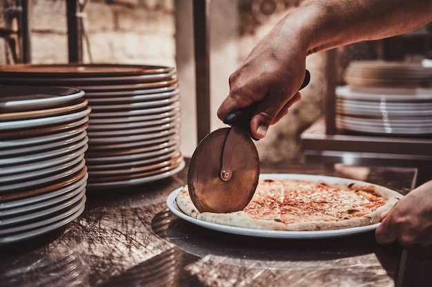 Photo gratuite un chef expérimenté coupe une pizza fraîchement préparée avec un couteau spécial.