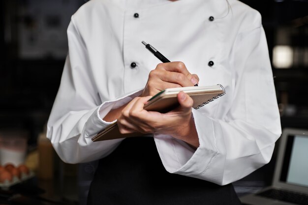 Chef féminin dans la cuisine prenant des notes avec un stylo et un cahier