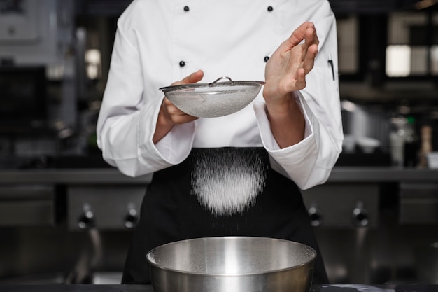 Chef féminin dans la cuisine tamisant la farine dans un bol