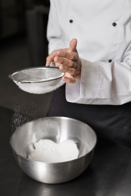 Photo gratuite chef féminin dans la cuisine tamisant la farine dans un bol