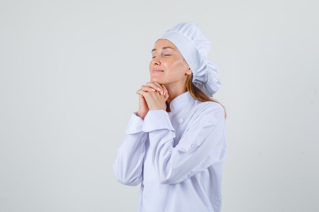 Chef féminin étayant le menton sur les mains jointes en uniforme blanc et à la recherche d'espoir.