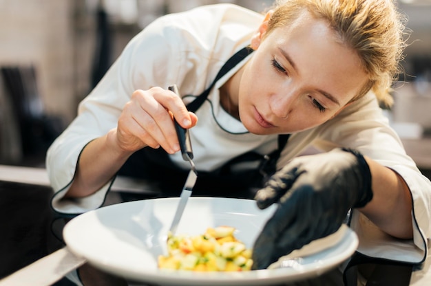 Chef féminin mettant de la nourriture sur une assiette