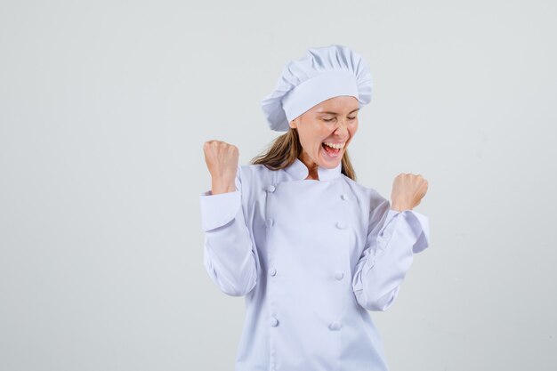 Chef féminin montrant le geste gagnant en uniforme blanc et à la recherche de plaisir. vue de face.