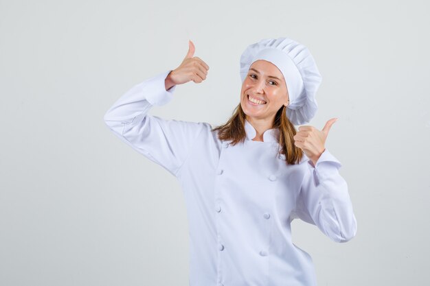 Chef féminin montrant les pouces vers le haut en uniforme blanc et l'air heureux. vue de face.