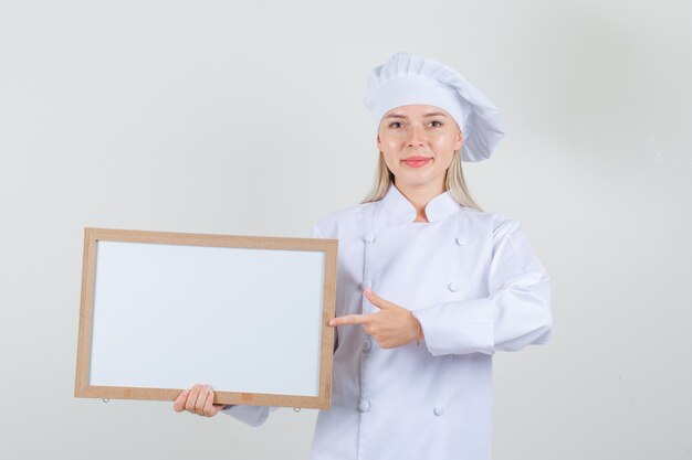 Chef féminin pointant le doigt au tableau blanc en uniforme blanc et à la joyeuse.