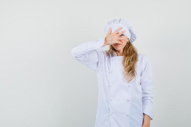 Chef féminin regardant à travers les doigts en uniforme blanc et à la honte