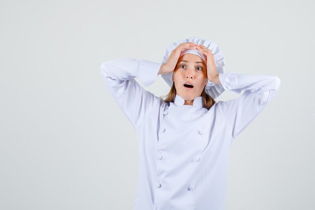 Chef féminin tenant les mains sur la tête en uniforme blanc et à la surprise