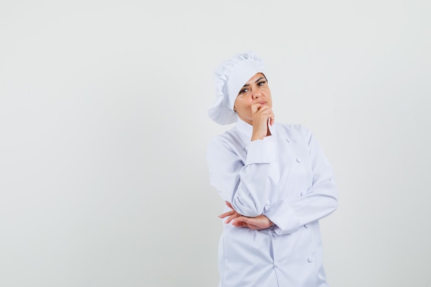 Chef féminin en uniforme blanc debout dans la pensée pose et à la recherche sensible