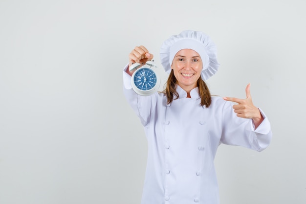 Chef féminin en uniforme blanc pointant le doigt au réveil et à la bonne humeur