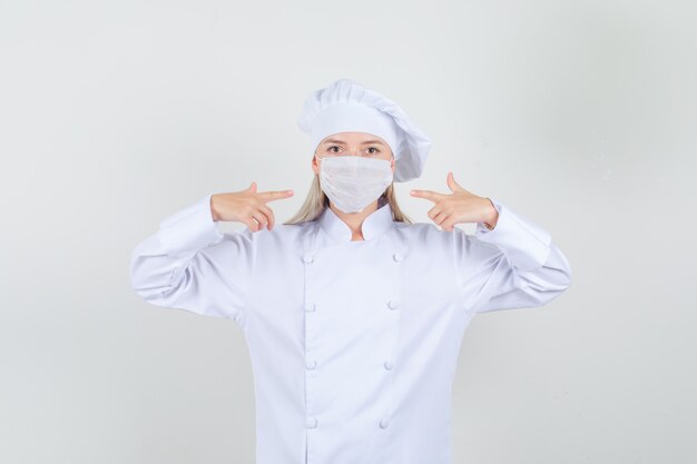 Chef féminin en uniforme blanc pointant du doigt au masque médical