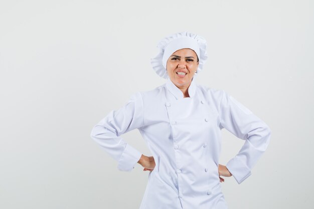 Chef féminin en uniforme blanc tenant les mains sur la taille et à la gaieté