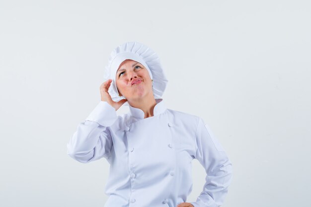 Chef de femme posant comme parler au téléphone tout en pensant en uniforme blanc et à la recherche concentrée