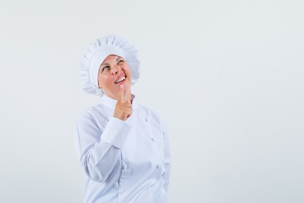 Chef de femme en uniforme blanc montrant un geste d'une minute et à la recherche d'un espace pensif pour le texte