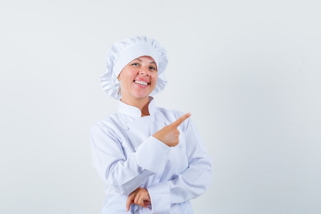 Chef de femme en uniforme blanc pointant vers le coin supérieur droit et à la joyeuse