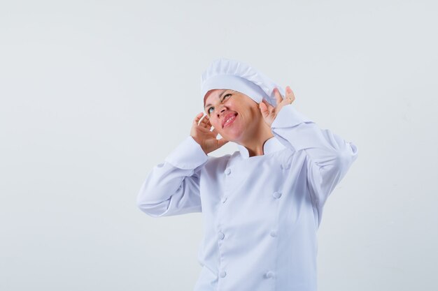 Chef de femme en uniforme blanc posant comme porter des écouteurs et à amusé