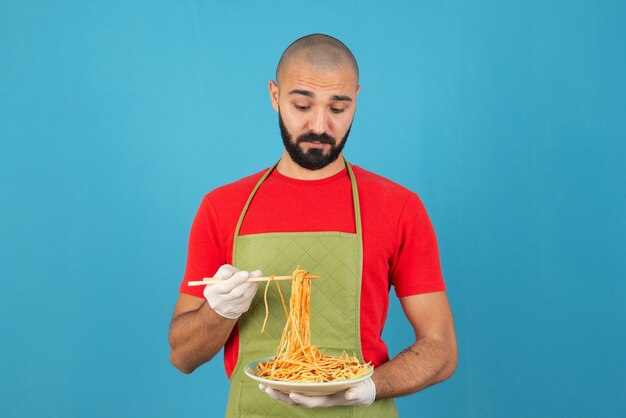 Chef masculin barbu en tablier et gants tenant une assiette de délicieux spaghettis.