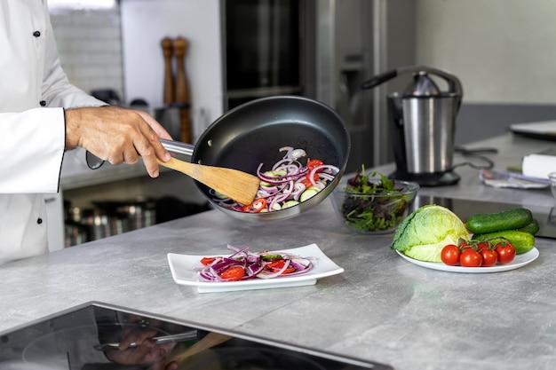 Chef masculin dans la cuisine versant de la nourriture sur une assiette à partir d'une poêle à frire