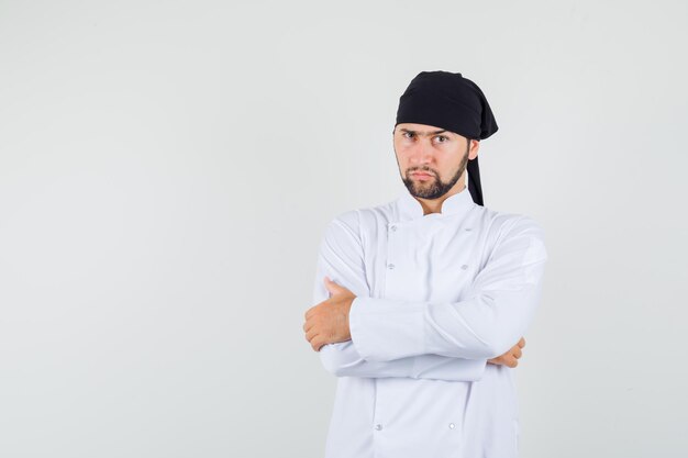 Chef masculin debout avec les bras croisés en uniforme blanc et l'air pensif. vue de face.