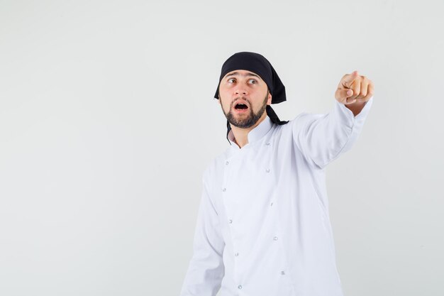 Chef masculin pointant vers quelque chose de loin en uniforme blanc et l'air inquiet, vue de face.