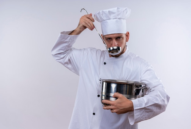 Chef masculin professionnel cuisinier en uniforme blanc et chapeau de cuisinier tenant une casserole de dégustation de nourriture avec une louche debout sur fond blanc