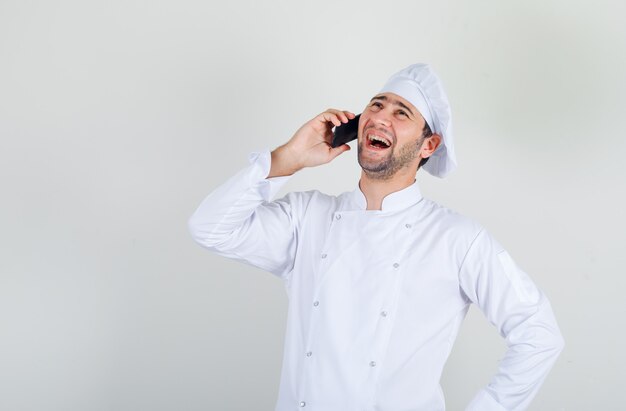 Chef masculin en riant tout en parlant au téléphone en uniforme blanc